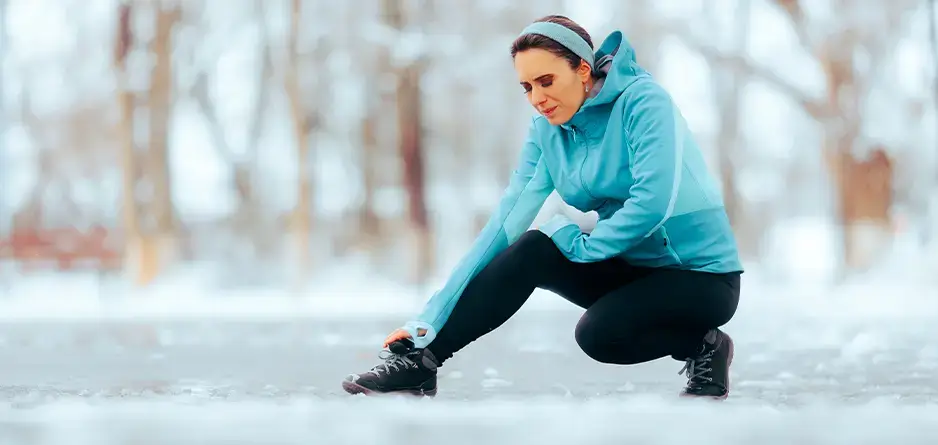 A runner in the snow holding her leg in pain due to leg cramps